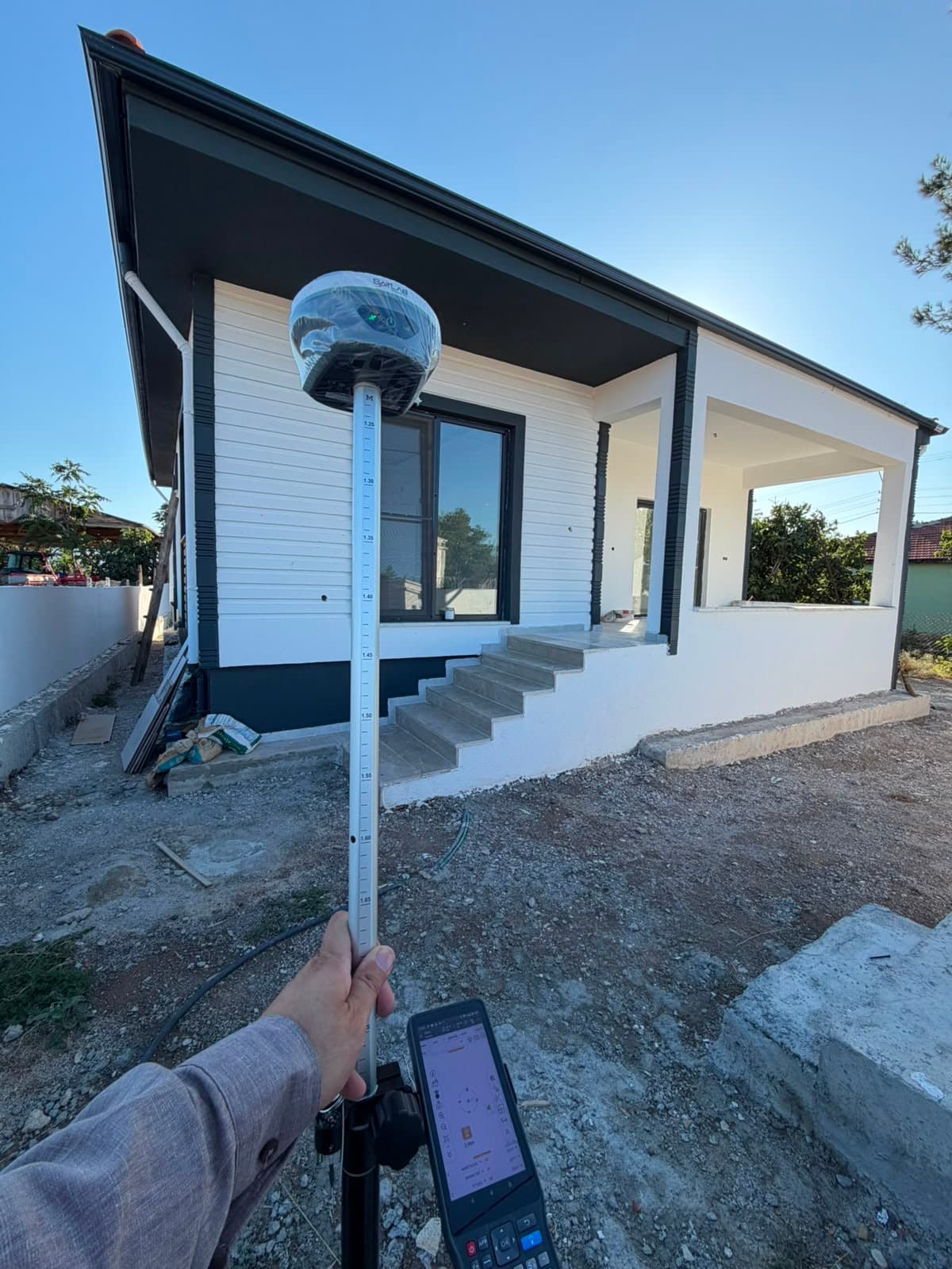 Yeni yapılmış bir evin önünde GNSS anteni ve el terminaliyle yapılan ölçüm çalışması